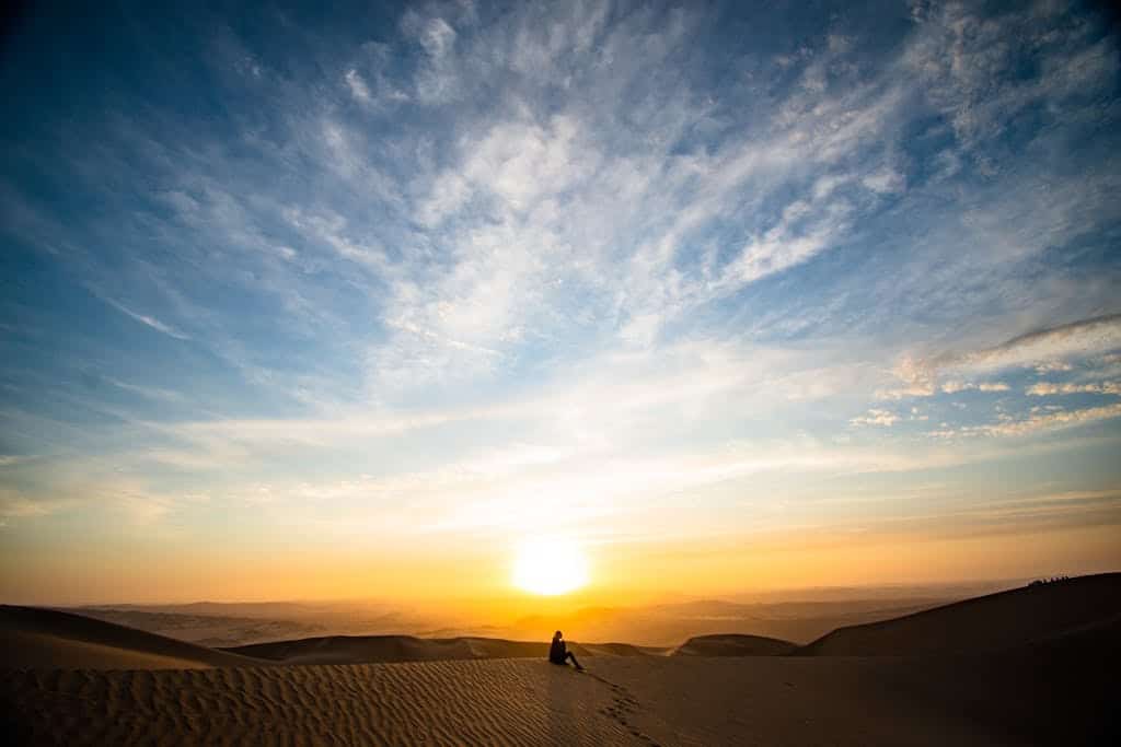 A stunning sunset over desert dunes in Paracas, Peru, with a solitary silhouette capturing tranquility.