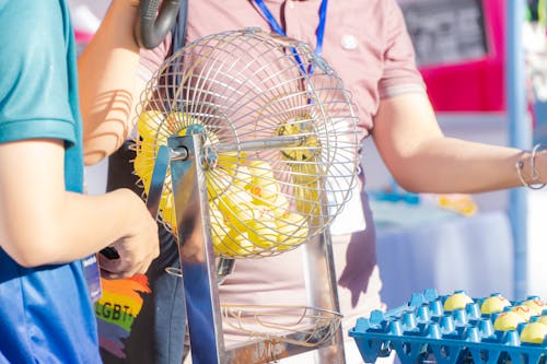 Two people engaging in a bingo game, spinning a cage in a lively, outdoor setting.