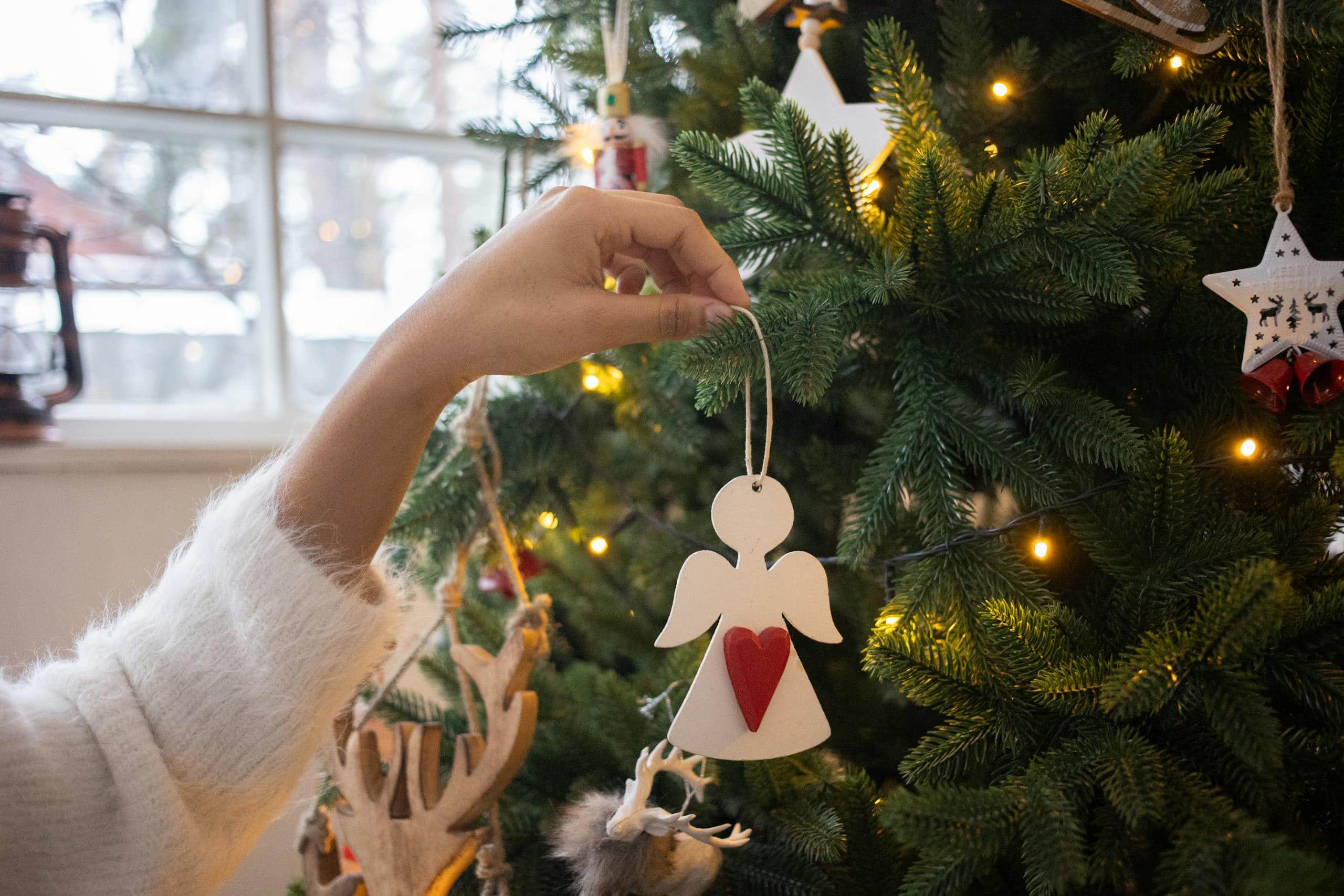 Close-up of a hand placing an angel ornament on a Christmas tree indoors.